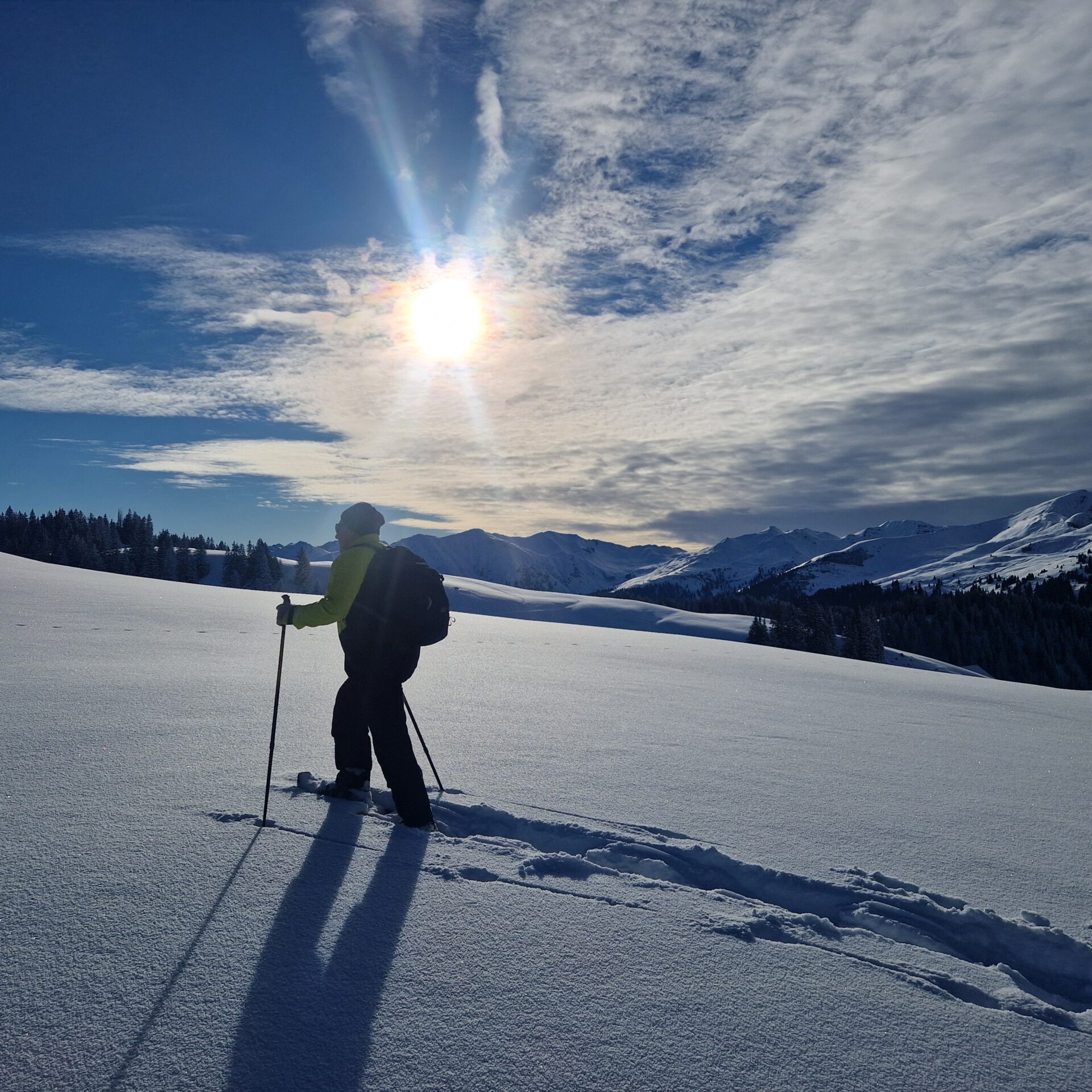 Mann läuft mit Schneeschuhen im Tiefschnee der Sonne entgegen