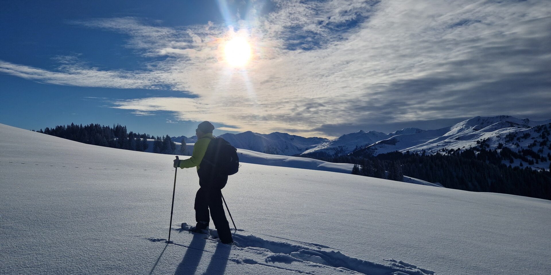 Mann läuft mit Schneeschuhen im Tiefschnee der Sonne entgegen