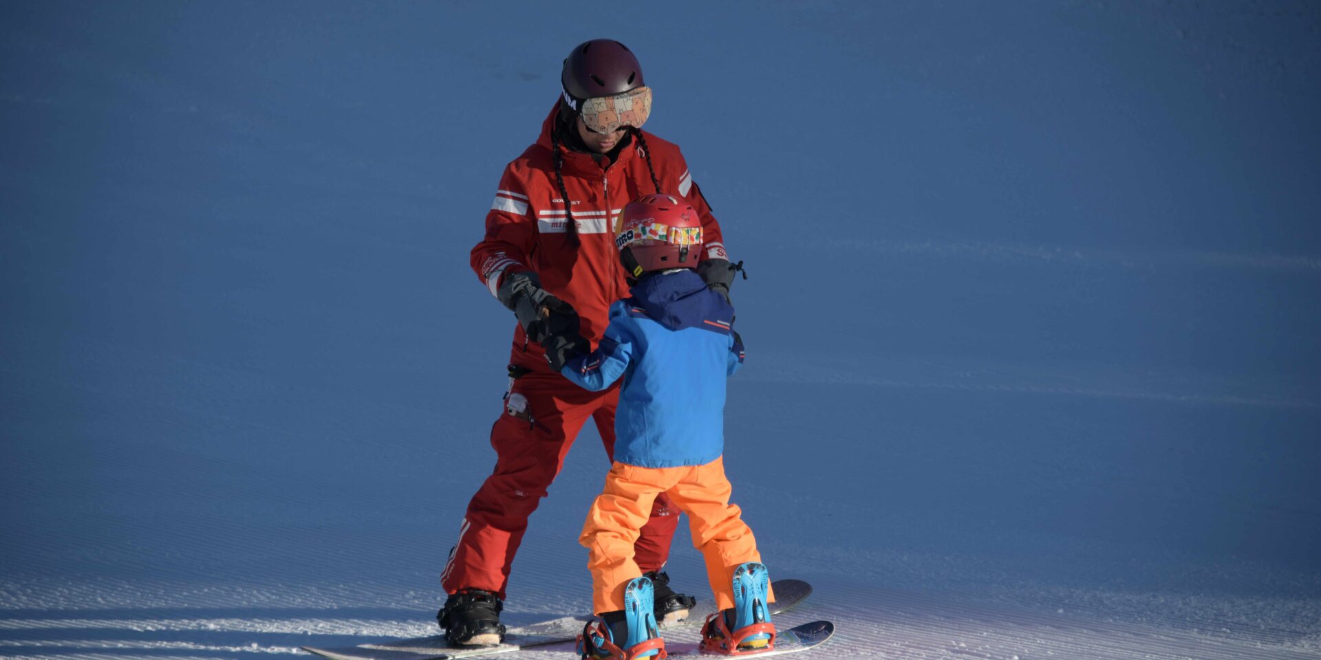 Skilehrerin fährt mit kleinem Kind auf dem Snowboard, Hand in Hand