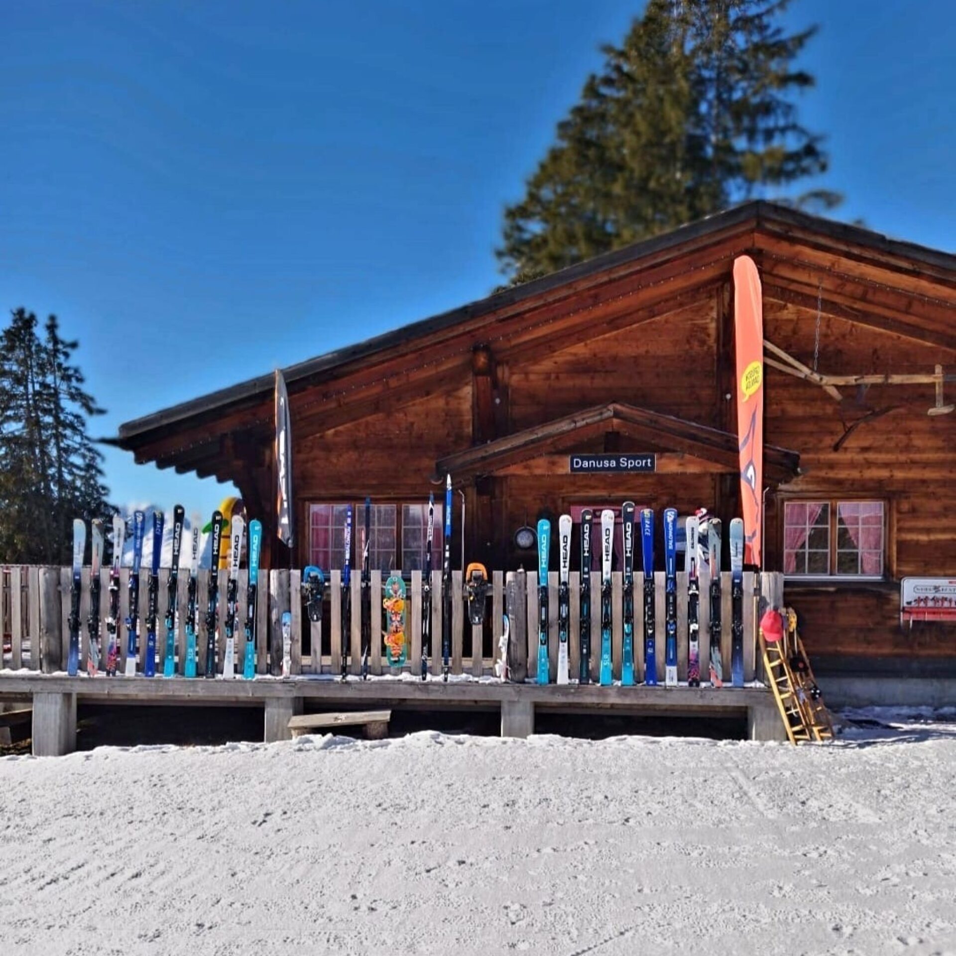 Danusa Sport auf dem Berg, Frontansicht mit vielen Ski und Sportartikeln auf der Terrasse aufgereit