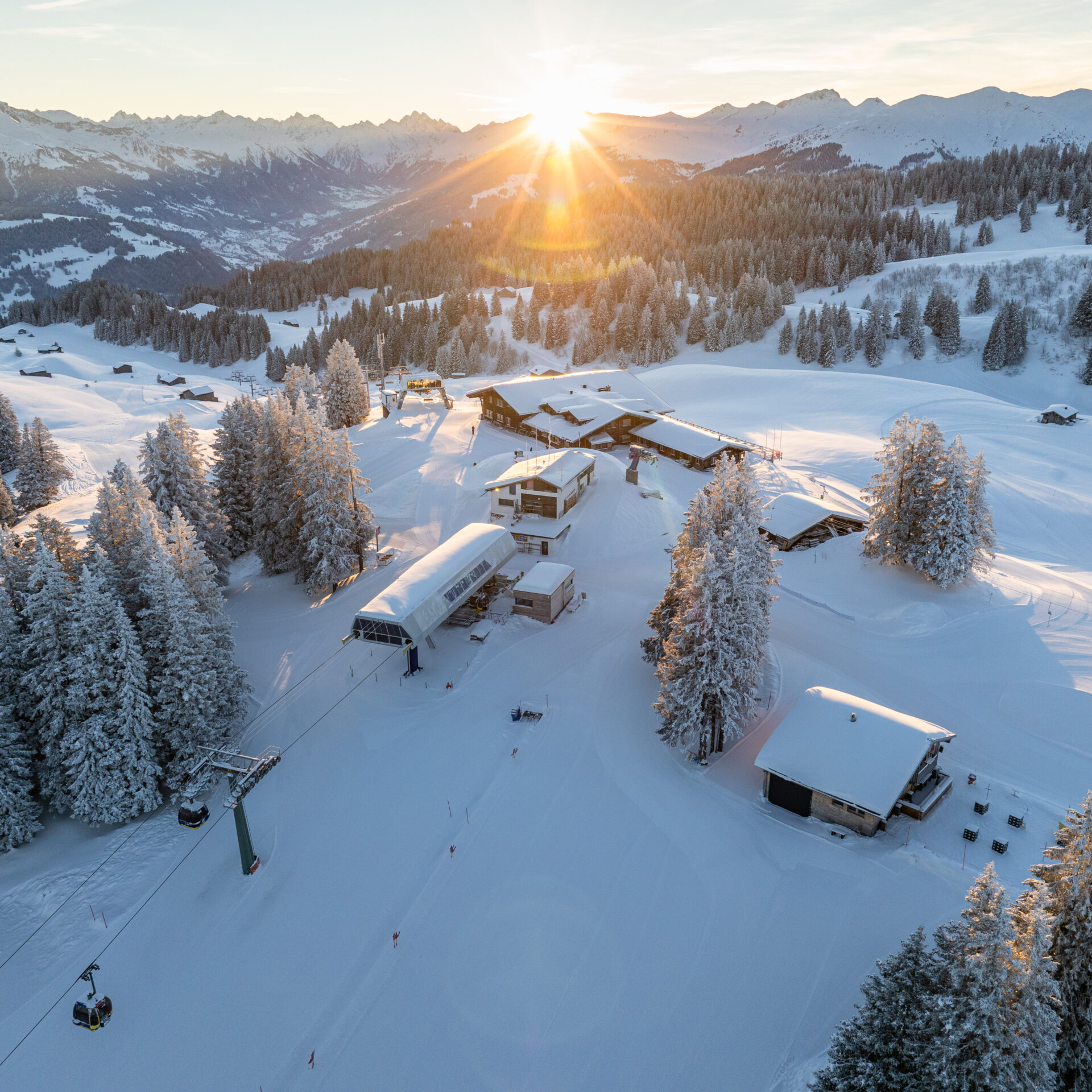 Drohnenansicht verschneites Skigebiet mit Sonnenaufgang im Hintergrunnd