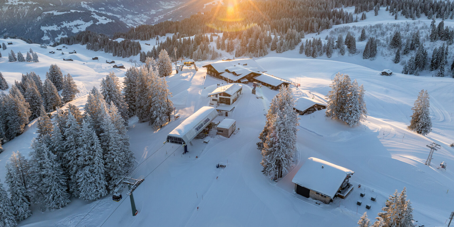 Drohnenansicht verschneites Skigebiet mit Sonnenaufgang im Hintergrunnd